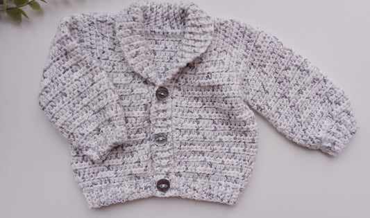 A light gray and white marled crochet cardigan sweater with three dark buttons, laid flat on a light gray background.