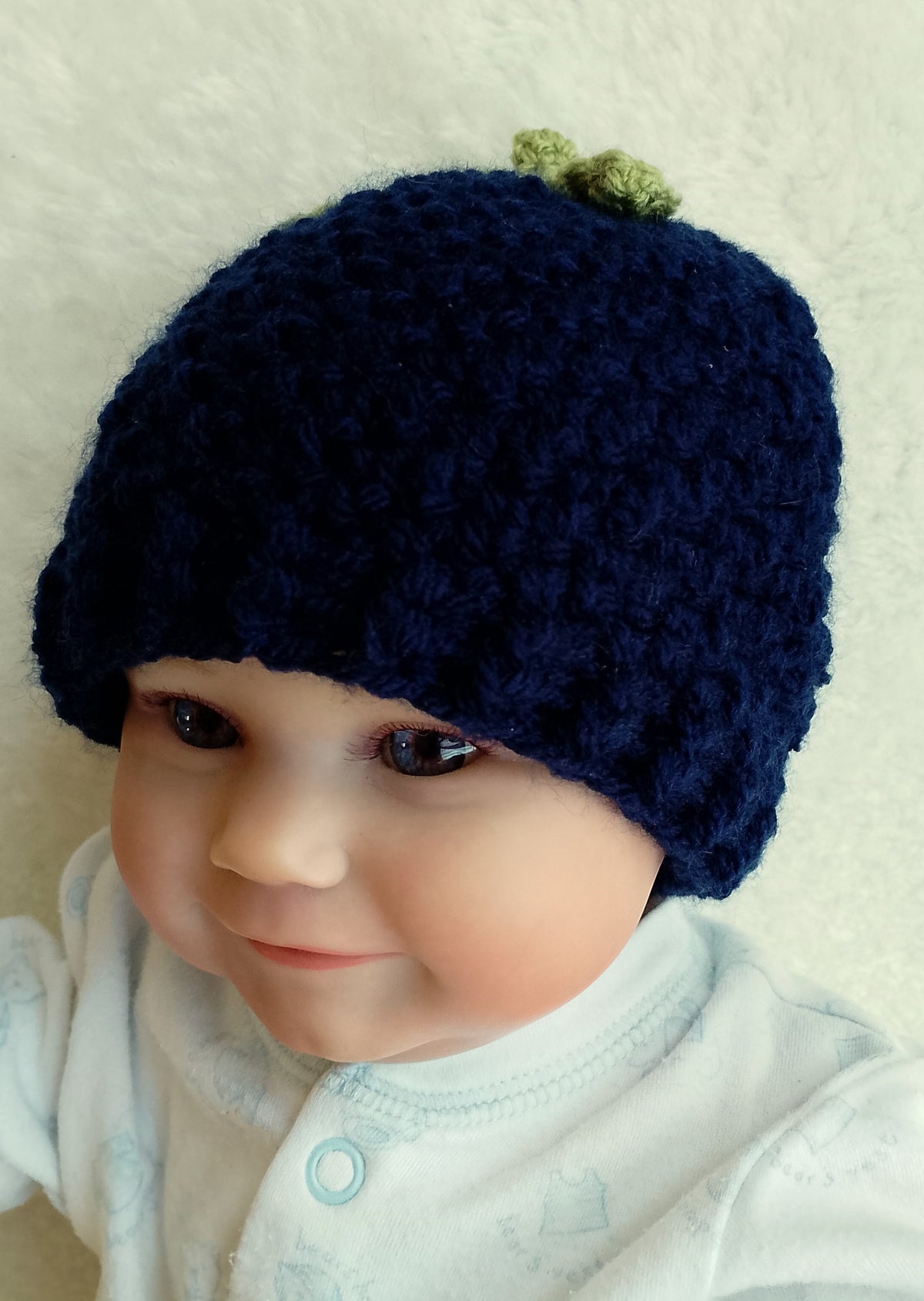 A close-up of a baby wearing a dark navy blue crocheted beanie with a small green leaf detail on top -blueberry hat photo prop