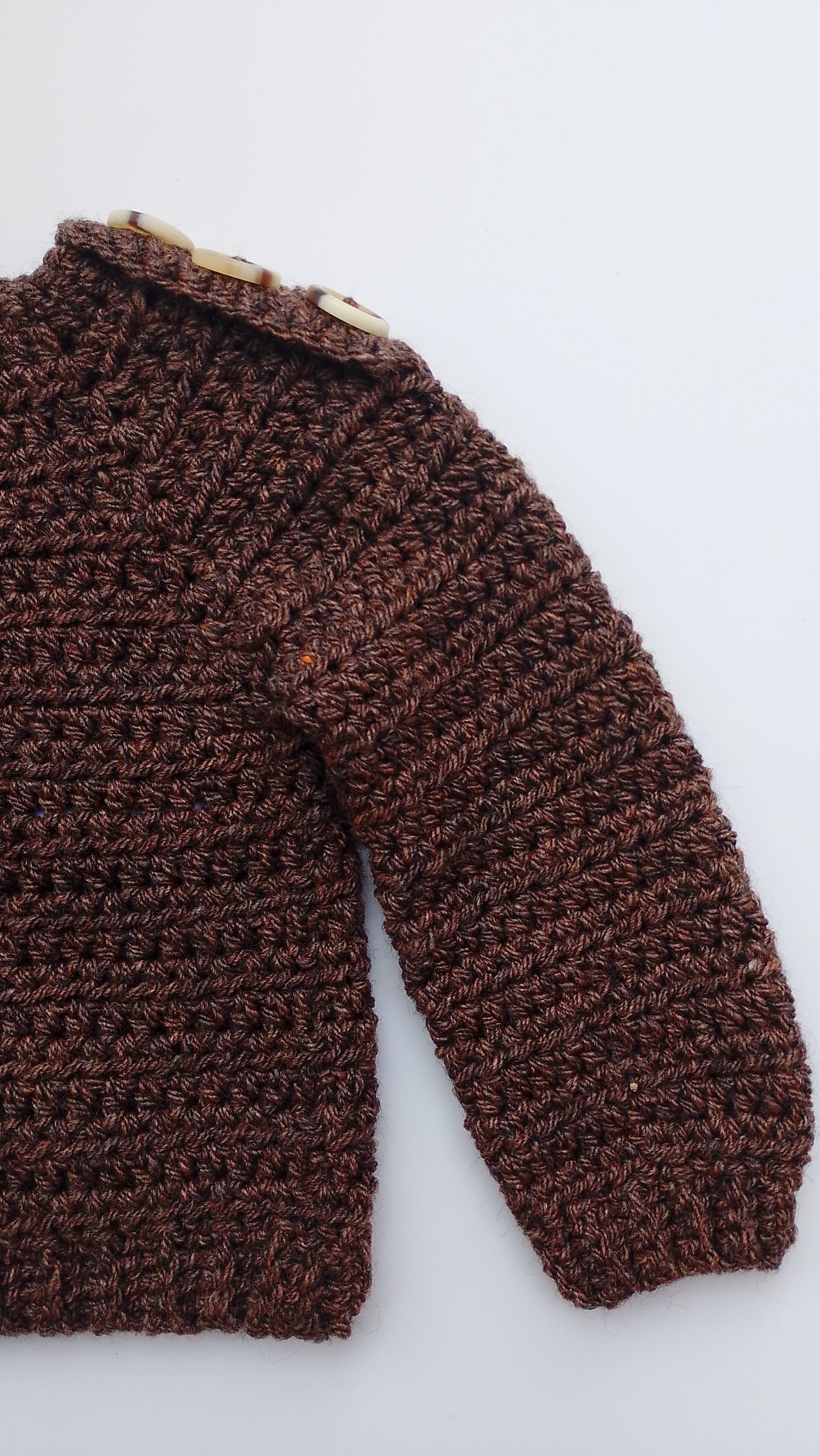 A close-up of a dark brown crochet pullover with a circular neckline and button fastening laid flat on a light gray background.