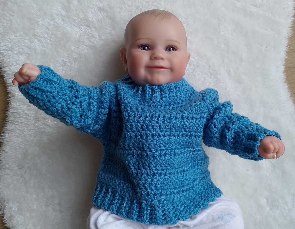 A baby doll or toy baby wearing a bright blue crocheted sweater, lying on a white faux fur surface.