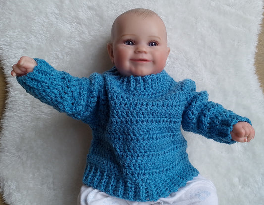A baby doll or toy baby wearing a bright blue crocheted sweater, lying on a white faux fur surface.