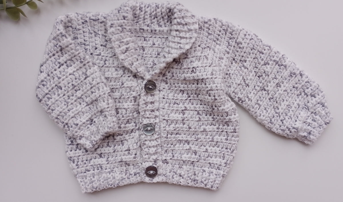A light gray and white marled crochet cardigan sweater with three dark buttons, laid flat on a light gray background.