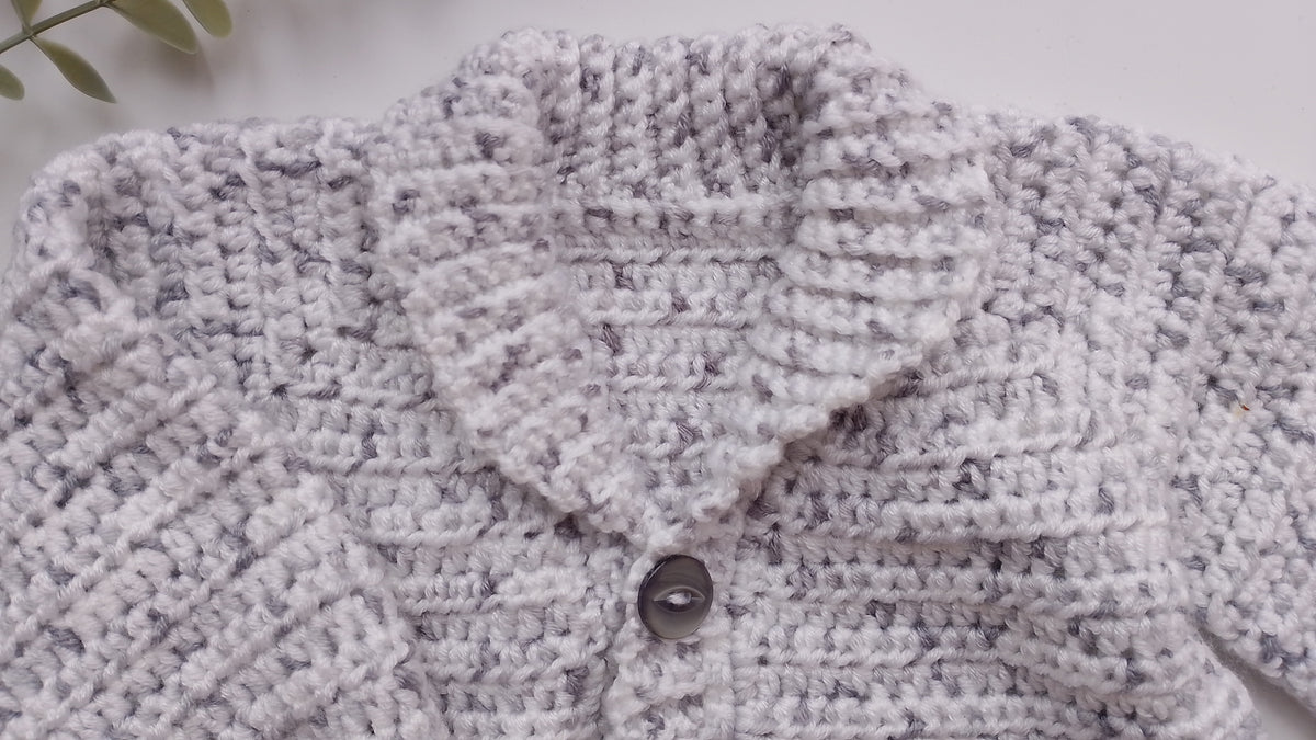 Close-up of a hand-crocheted cardigan in a heathered white and light gray yarn, featuring a single dark gray button closure.